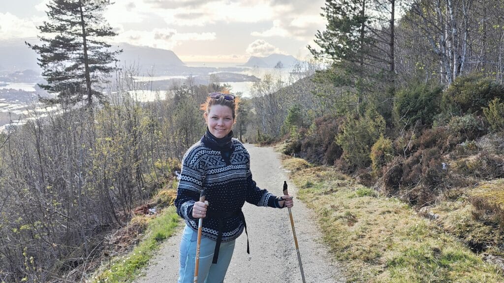 Bilde av Annette Madsen Arnestad som står på en tursti med utsikt over fjord og fjell.