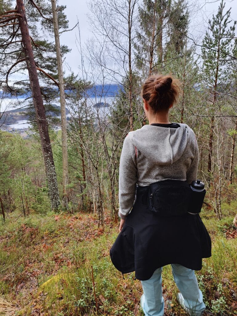 Bilde av Anette Madsen Arnestad som står ute i skogen med ryggen til kamera.