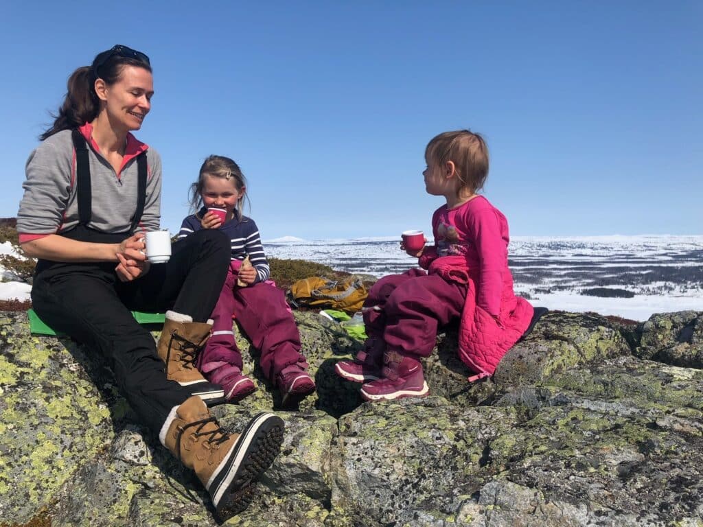 Bilde av Miia og hennes to døtre som sitter på et fjell med en blå himmel som bakgrunn.