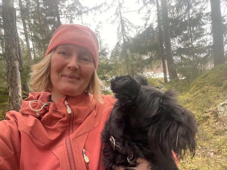 Bilde av Eris Horten Steig og hennes sorte hund ute i skogen. Eris er likeperson i MS-forbundet.